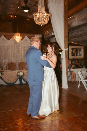 A couple shares their first dance at a wedding reception under elegant crystal chandeliers in a rustic venue with draped decor.