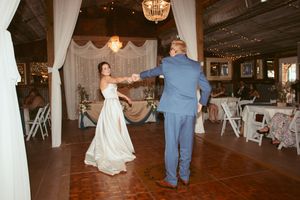 A wedding celebration in a rustic barn venue with white draping, chandeliers and wooden floors during a dance.