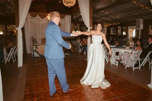 Couple dances together at their wedding reception in a rustic barn venue with string lights and white decor.