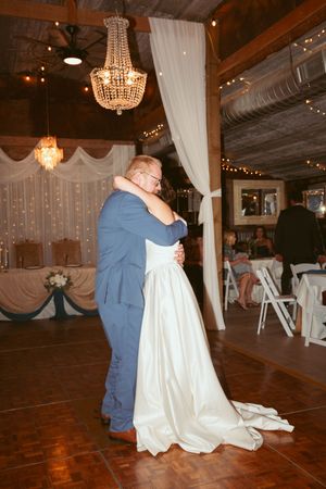 A couple dances together in a rustic venue with wooden floors and elegant crystal chandeliers.