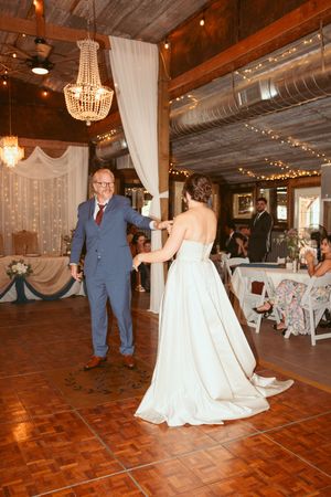 Wedding reception dance in a rustic venue decorated with string lights and elegant chandeliers.