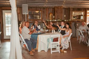 Wedding guests relax and socialize at rustic wooden tables during a barn venue reception.