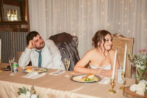 Two guests sit at an elegant dining table with candles and flowers, looking away from each other in opposite directions.