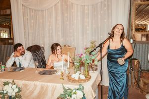 Wedding party wearing teal bridesmaid dresses poses together in rustic barn venue.