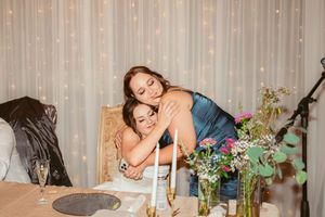 Two people embrace at an elegantly decorated dining table with twinkling lights and floral arrangements.