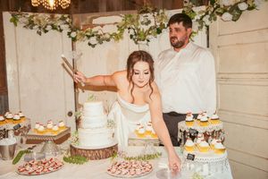 Wedding cake display table decorated with greenery garlands and desserts at rustic reception venue.