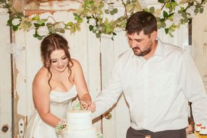 Bride and groom sharing a playful moment dancing together with decorative vines on white fence backdrop.