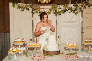 Wedding dessert table features white tiered cake and colorful cupcakes with floral decorations.