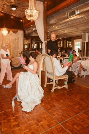 A wedding reception in a rustic venue decorated with crystal chandeliers and white drapes on a wooden dance floor.