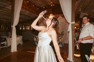 Couple shares first dance at rustic barn wedding reception with white drapes and twinkling lights in background.
