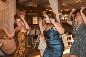 People dancing enthusiastically at a celebration in a rustic venue decorated with string lights.