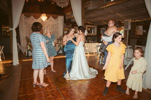 Couples dancing together on a wooden dance floor at an indoor wedding reception with white drapes and soft lighting.