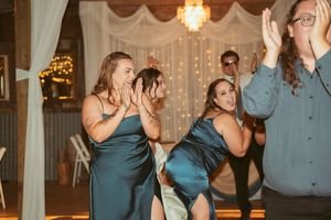 Wedding party members dancing and laughing together at a reception with twinkling lights and drapes in the background.