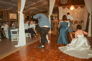 Wedding guests dancing energetically on a wooden dance floor decorated with white drapes and twinkling lights above.
