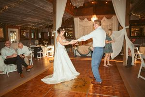 A wedding couple dancing together on a wooden dance floor decorated with white drapes and string lights.