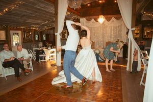 Wedding celebration with dancers on a rustic wooden floor under elegant white fabric draping and sparkling lights.