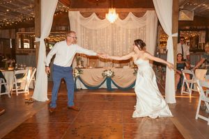 A joyful dance moment between two people at a rustic barn wedding reception with white drapes and wooden floors.