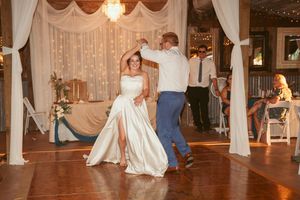 A couple dances together in an elegantly decorated reception hall with white drapes and twinkling lights.