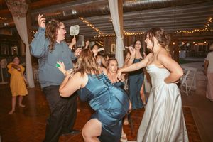 Wedding guests dancing energetically at a reception with string lights overhead in a rustic venue.