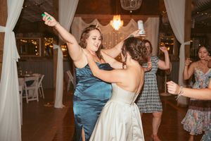 Wedding guests dance joyfully on a wooden dance floor decorated with string lights and white drapes.