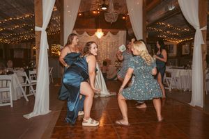 Party guests dancing and laughing together on a wooden dance floor decorated with string lights and white draping.