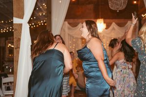 Wedding guests dancing and enjoying themselves at a reception with twinkle lights and white drapes.
