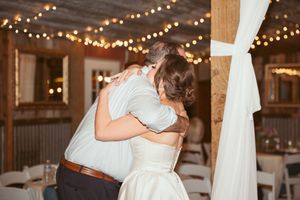 A tender embrace captured during a dance at a rustic wedding reception with twinkling lights overhead.