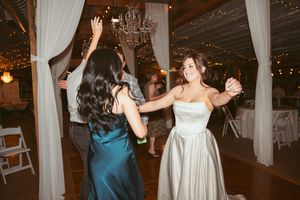 Joyous dance party at an indoor wedding reception decorated with white drapes and twinkling lights.