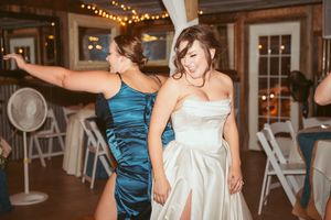 Wedding party dancing and celebrating in a rustic barn venue with decorative lighting.
