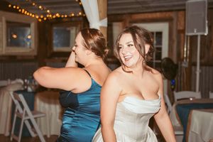 Wedding party members in teal bridesmaid dresses and formal attire dance together at indoor reception.
