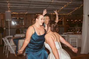 Wedding party celebration with dancing under strings of lights in a rustic indoor venue.