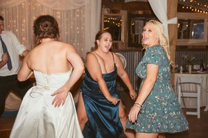 Wedding reception guests dancing together in formal attire under twinkling lights and white fabric decor.