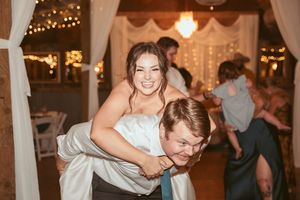 Dancing guests share lighthearted moments at a wedding reception under twinkling lights and white fabric decor.