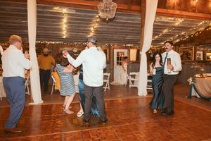 Multiple couples dance together on a wooden floor at an indoor reception with white pillars and twinkling lights.