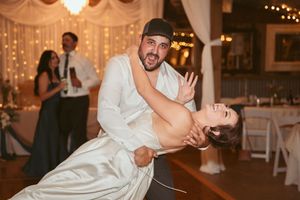 Couples enjoying energetic dancing at an indoor wedding reception with decorative lights and white drapes.