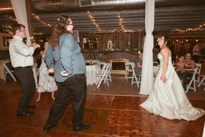 Wedding guests dance and celebrate on a rustic wooden dance floor decorated with string lights and white draping.