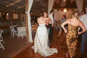 Wedding reception dance party in a rustic venue decorated with white drapes and string lights.