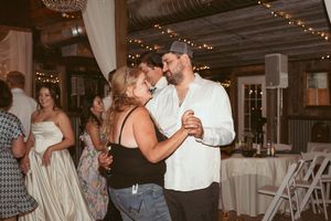 Couples dance together at a rustic wedding reception venue decorated with string lights and white drapes.