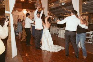 Wedding guests dancing and celebrating on a wooden dance floor adorned with white fabric and twinkle lights.