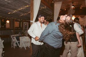 Guests dancing and celebrating at a rustic indoor wedding reception with string lights and white fabric decor.
