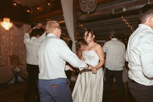 Couples dance at an evening wedding reception under warm lighting and decorative chandeliers.