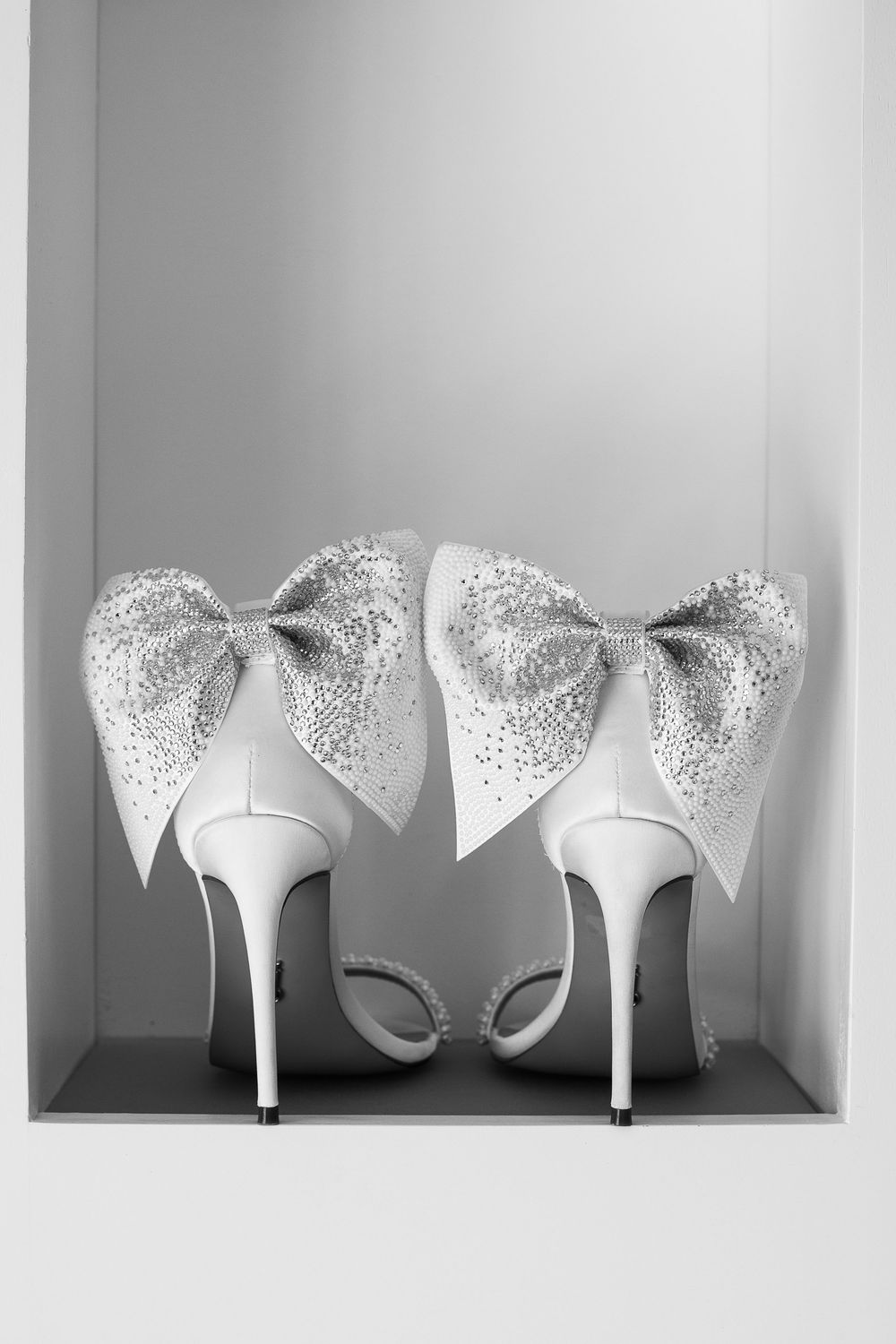 Elegant white high heel wedding shoes decorated with glittery silver bow detailing displayed in a showcase.