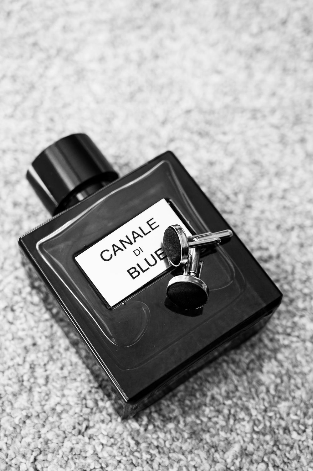 A black perfume bottle labeled 'Canale Blue' photographed in black and white on a textured surface.
