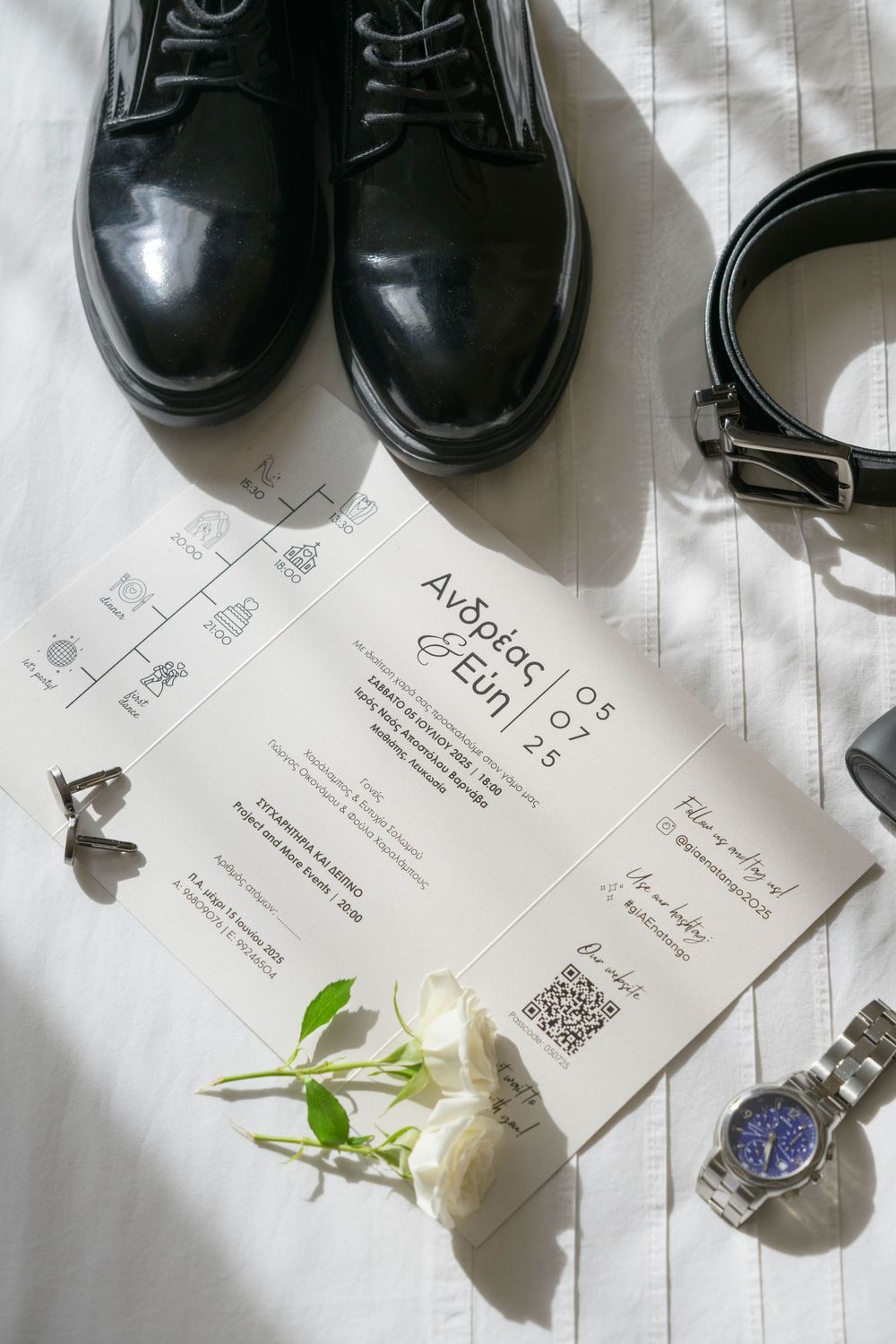 Wedding details flatlay with black dress shoes, watch, white rose and invitation card.