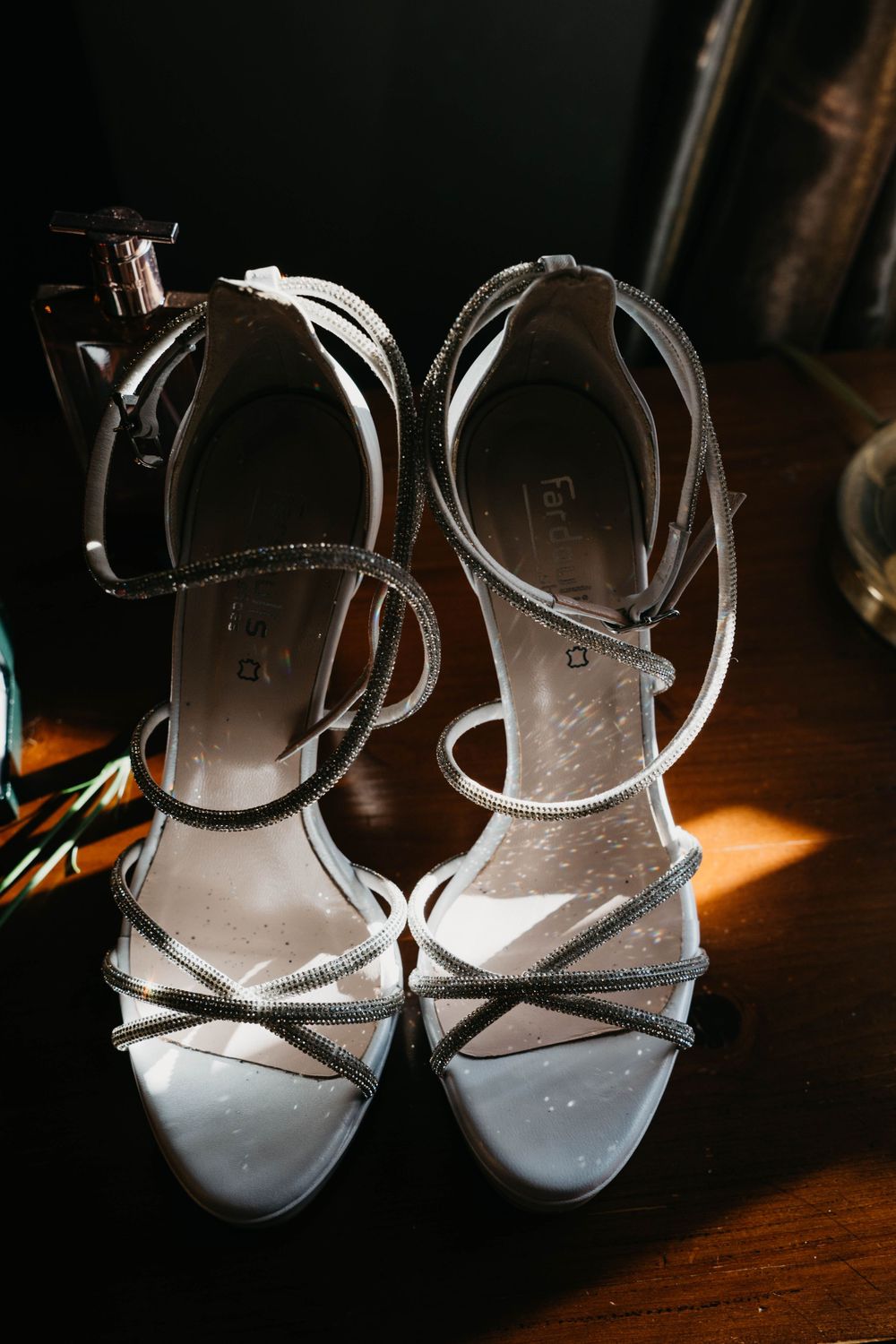Elegant silver strappy wedding heels on a dark wooden surface.