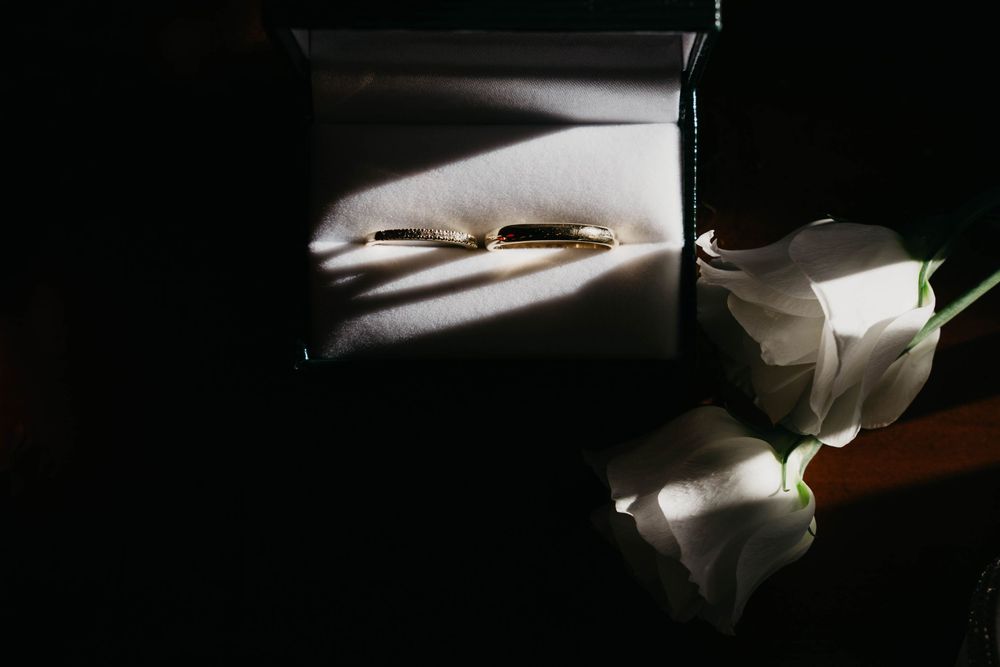 Dramatic lighting on wedding rings with white roses in the background.