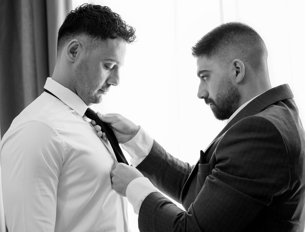 Two men in formal attire preparing for an event in black and white photography.