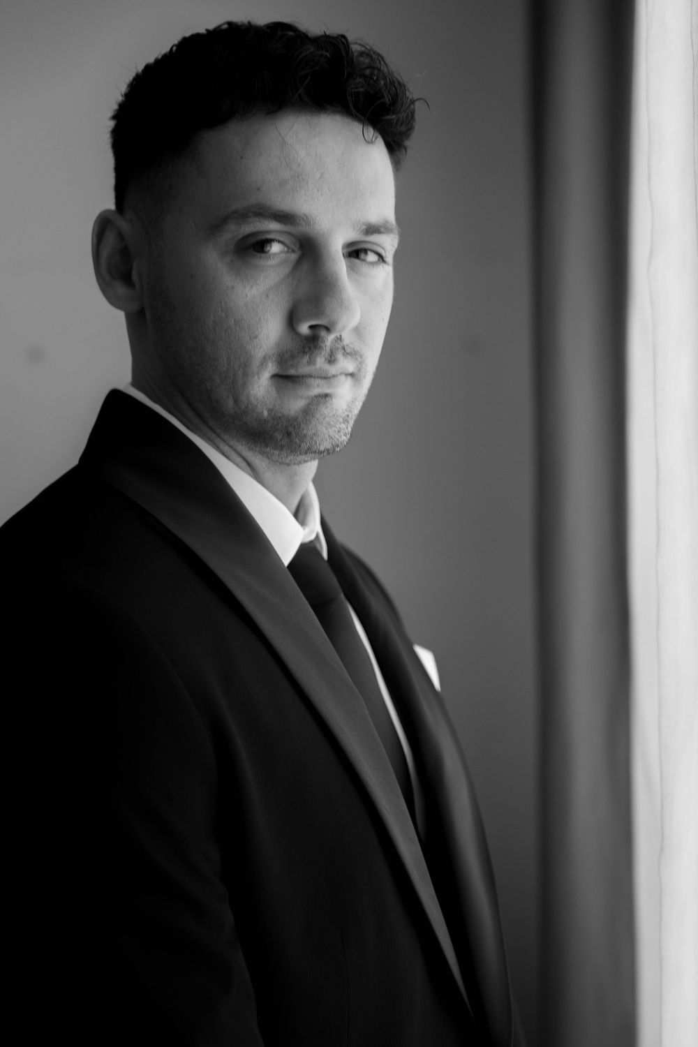 Dramatic black and white portraits of person in suit against window lighting.