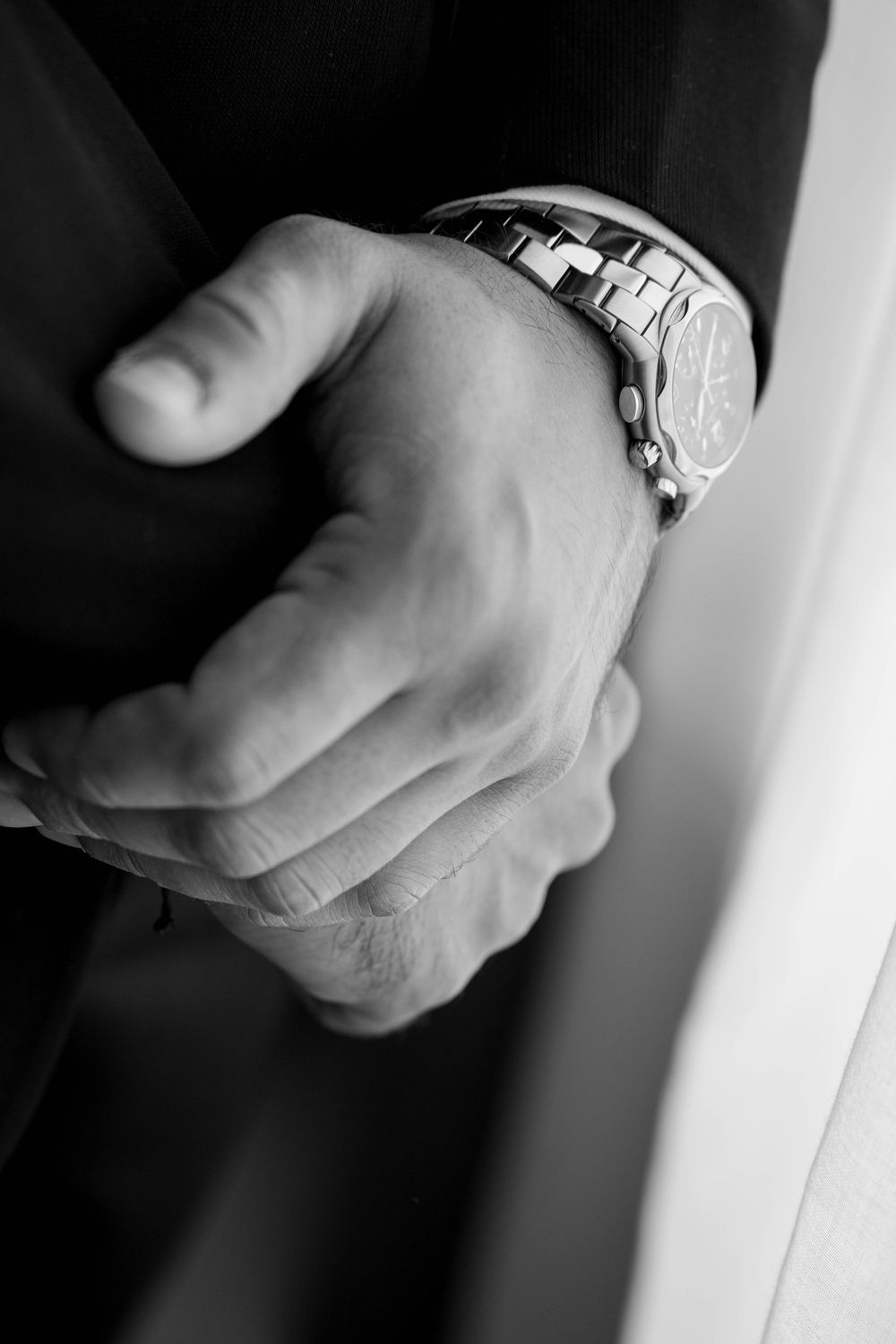 Close-up black and white shots of hands with watch and formal attire.
