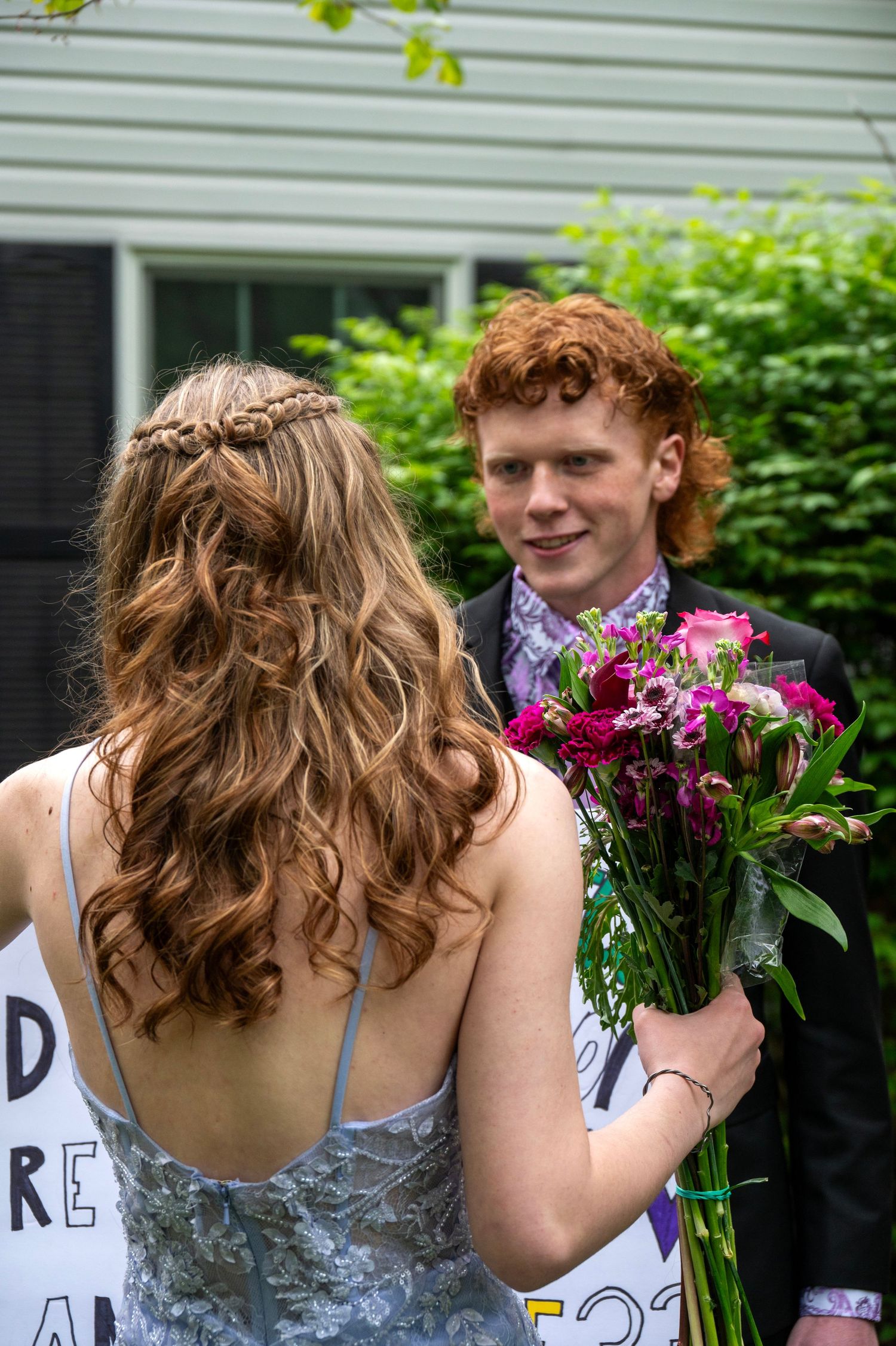 A silver-dressed person receives a vibrant purple and pink bouquet of flowers in a garden setting.
